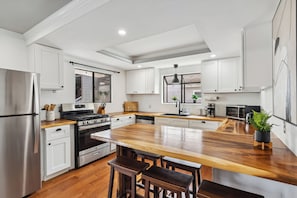 Cozinha moderna com armários brancos, bancada de madeira e eletrodomésticos de aço inoxidável.