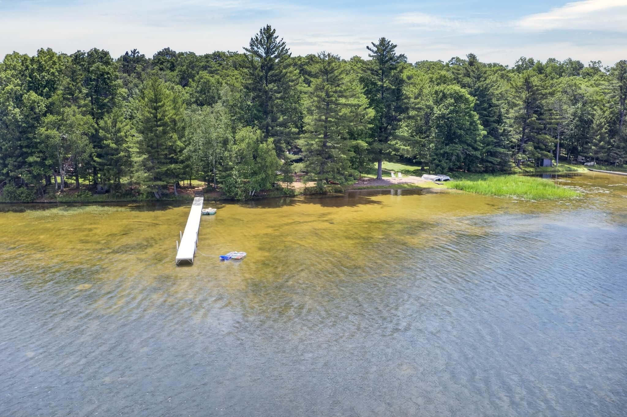 A river with a wooden dock extending into the water, surrounded by dense forest.