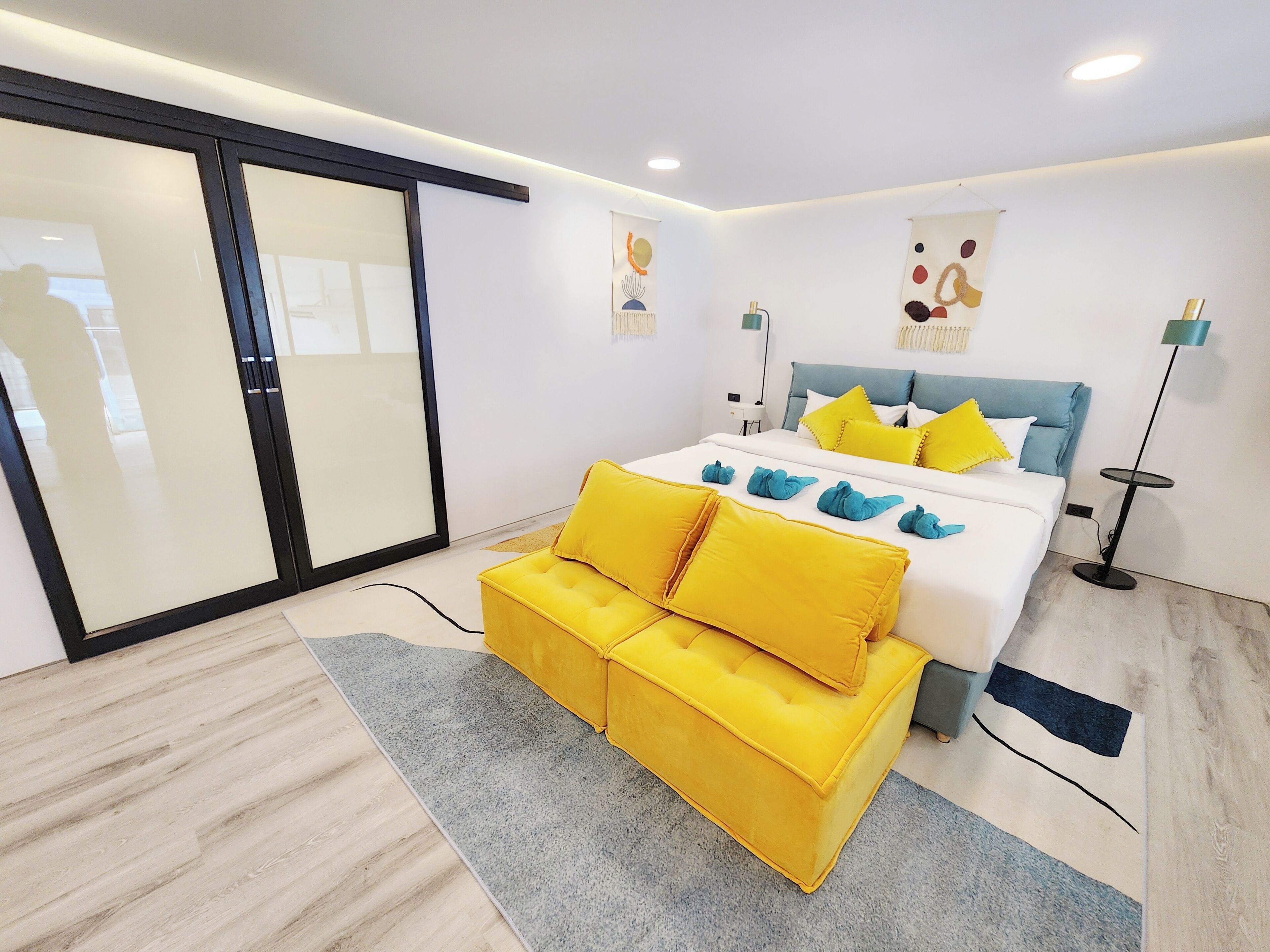A modern bedroom with a bed, a yellow sofa, a floor lamp, and a large window.