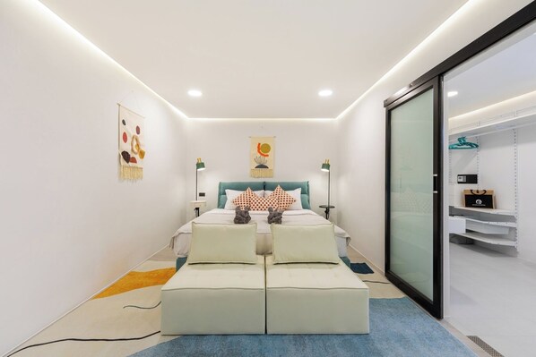 A modern bedroom with a bed, bedside tables, and a glass door leading to a storage area.