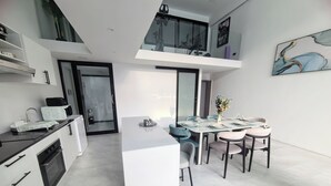 A modern kitchen with a central island, a dining area with a glass-top table, and a view of the city through large windows. - Unique Pool Slide Access Townhouse (Bophut)