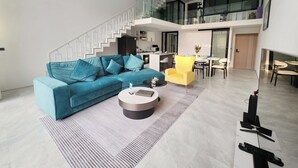 A modern living room with a blue sofa, a yellow armchair, and a coffee table. A staircase leads to an upper level. - Unique Pool Slide Access Townhouse (Bophut)