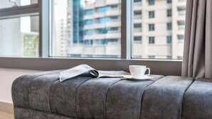 Un banco tapizado gris con un periódico y una taza blanca.