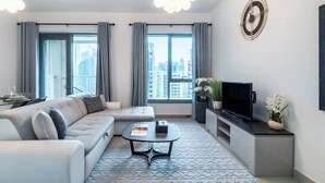 Una sala de estar moderna con sofá, mesa de centro, televisor y ventanas grandes con cortinas.