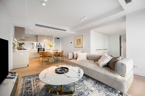 A modern living room with a sofa, coffee table, and a dining area with chairs and a table.