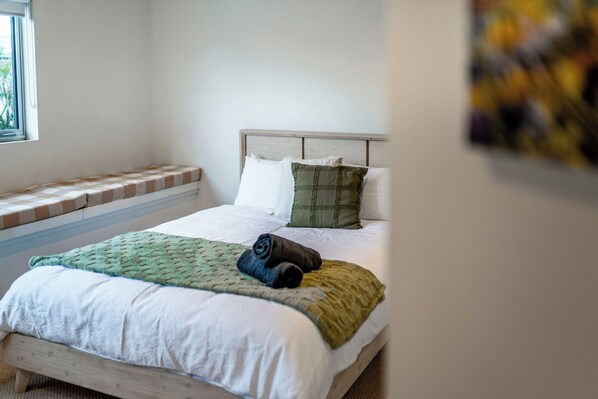 A neatly made bed with a green and white quilt, a rolled towel, and a green plaid pillow.
