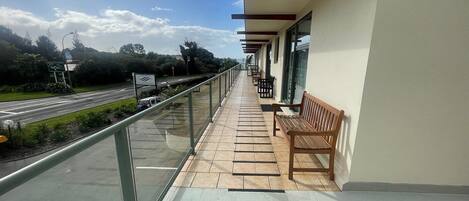 A balcony with a bench, a glass railing, and a view of a road and greenery.