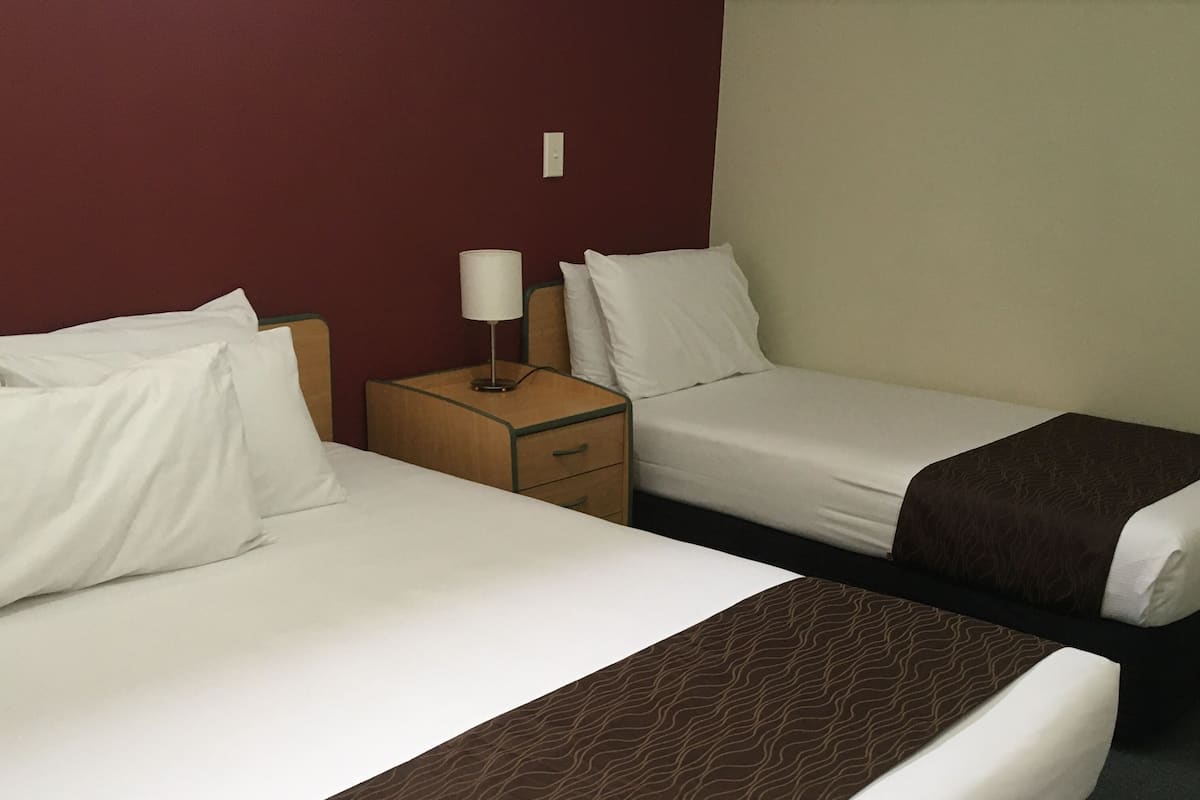 A hotel room with two beds, a nightstand, and a lamp.