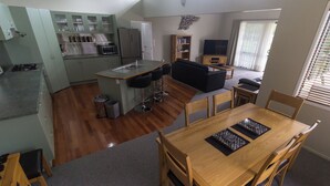 Une cuisine moderne dotée d’un îlot central, un coin repas avec une table et des chaises en bois, et un salon avec un canapé et un téléviseur.