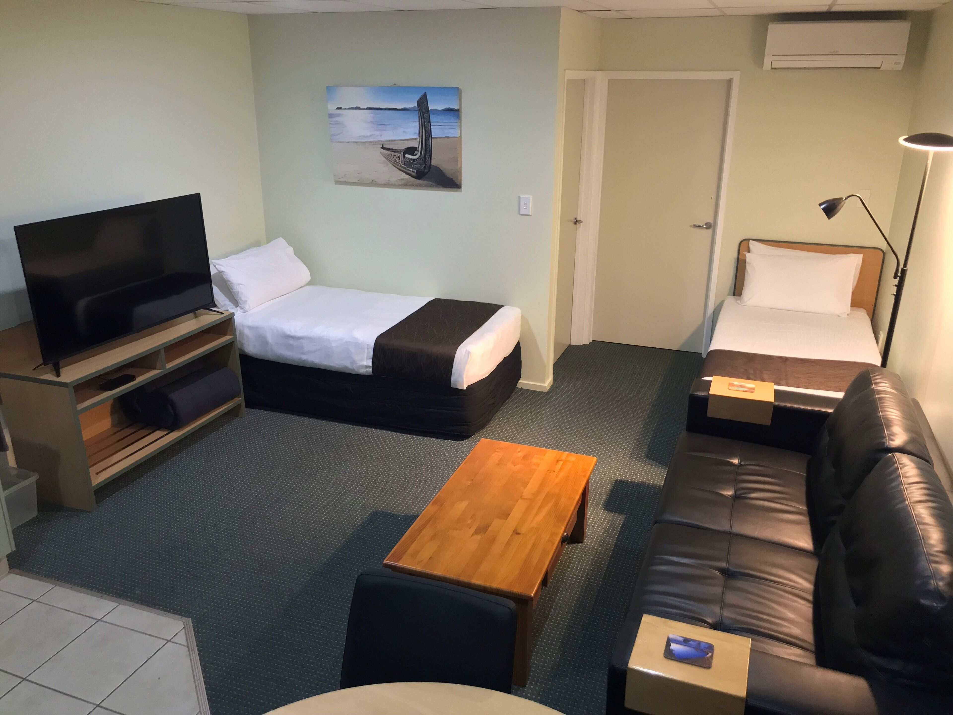 A hotel room with a bed, a sofa, a TV, a desk, and a painting on the wall.