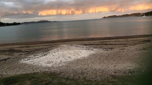 Un paysage côtier avec une vaste plage, une eau calme et des collines lointaines sous un ciel nuageux.