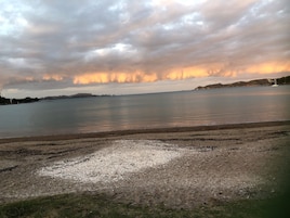 Un paisaje costero con una playa extensa, agua tranquila y colinas lejanas bajo un cielo nublado.