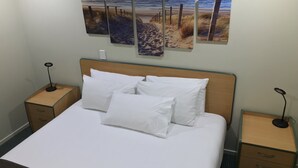 A neatly made bed with white linens and pillows, a wooden headboard, and bedside tables with lamps. - Bay of Islands Gateway Motel & Apartment (Paihia)
