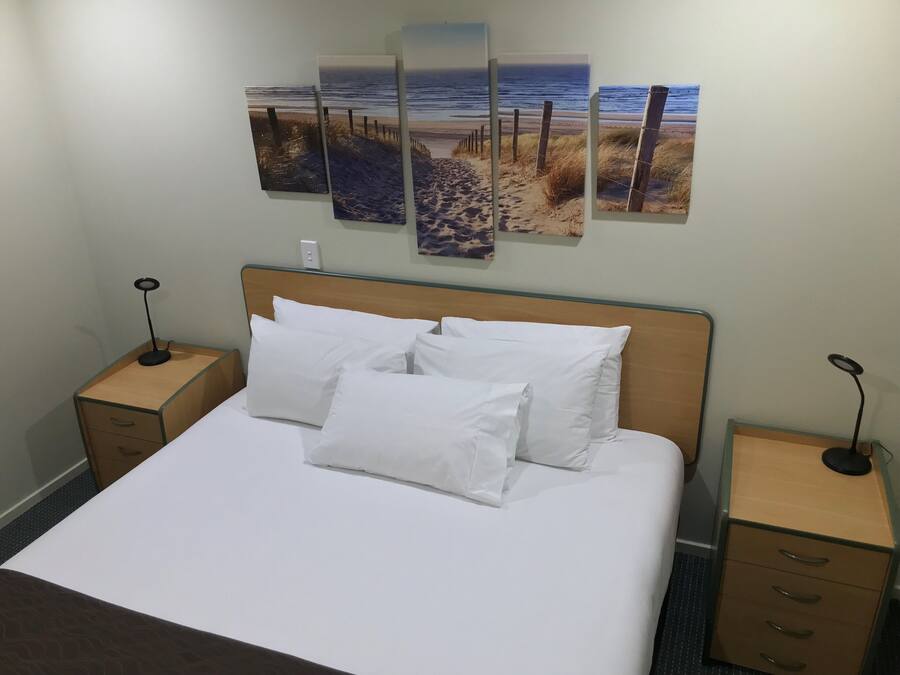 A neatly made bed with white linens and pillows, a wooden headboard, and bedside tables with lamps.