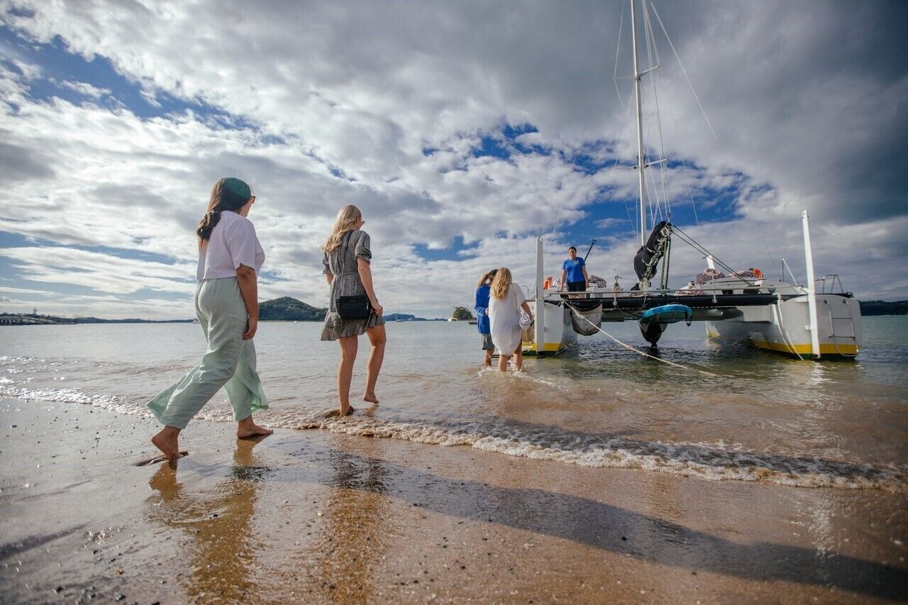 A group of people walking towards a boat on a beach with a partly cloudy sky.