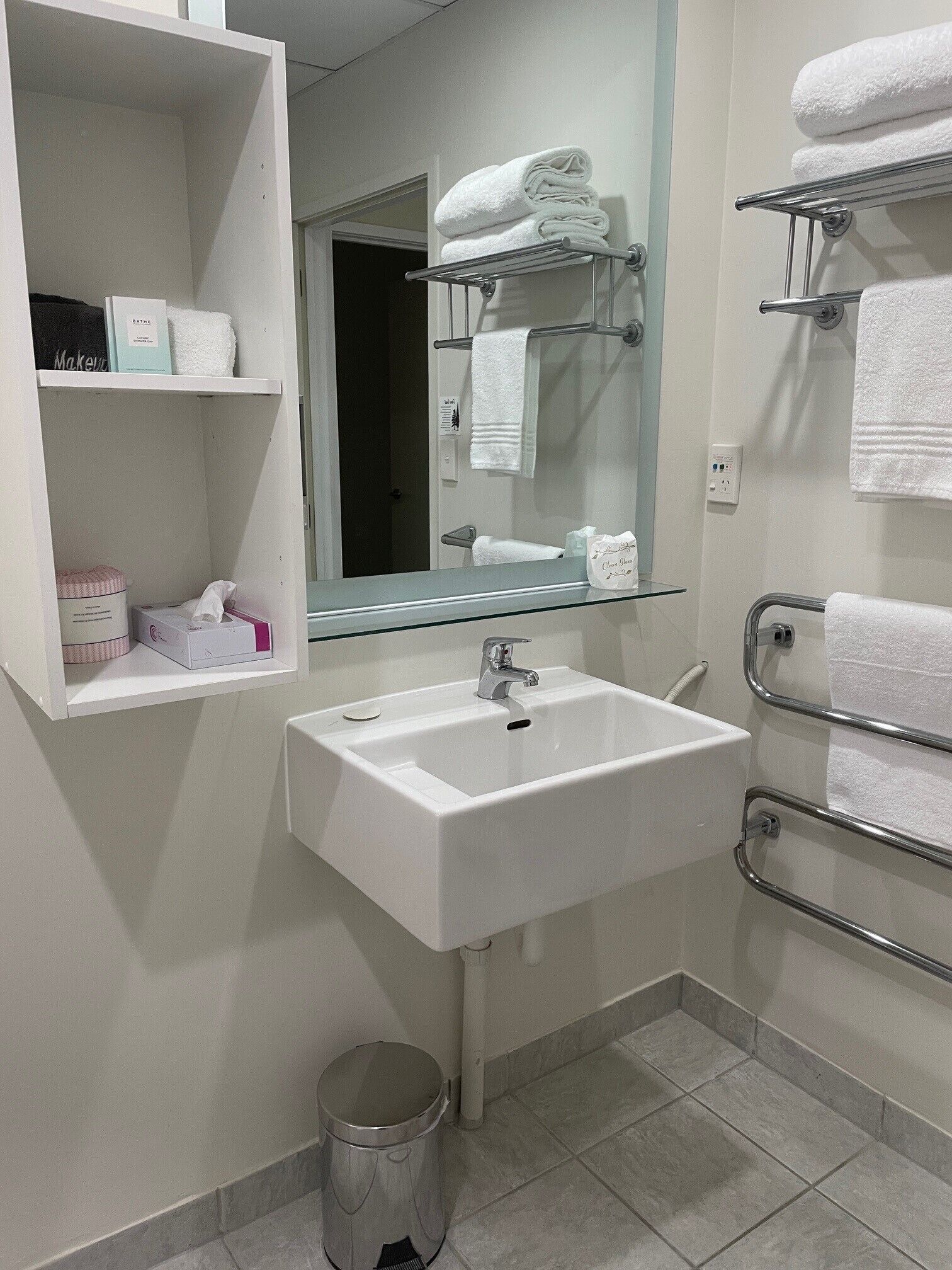 A bathroom with a white sink, a mirror, a towel rack, and a shelf with toiletries.