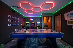 Una mesa de billar con luces de neón, máquinas de videojuegos y carteles que indican 'Whistle Pig' y 'Sky Bar'.