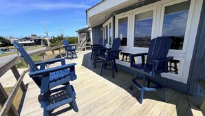 A deck with chairs and tables, overlooking a body of water and buildings.
