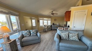 A spacious living room with two grey sofas, a wooden coffee table, and a dining area with a table and chairs.
