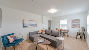 A modern living room with a sofa, a blue armchair, a coffee table, and a dining area with chairs and a table. - Charming Modern Cottage, Downtown @pinpointstays (Coos Bay)