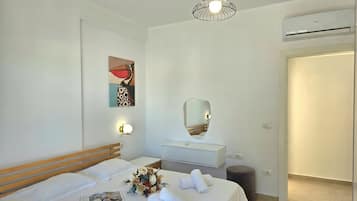 A hotel room with a bed, bedside table, mirror, wall art, and an air conditioning unit.