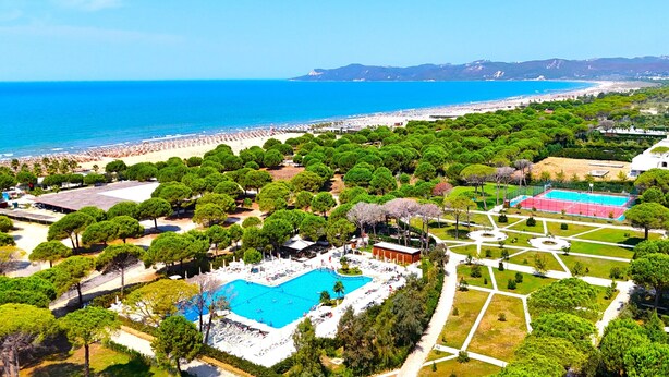 An aerial view of a resort with a swimming pool, beach, and landscaped areas.