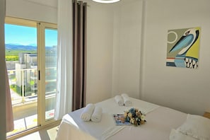 A hotel room with a bed, towels, a magazine, and a painting.