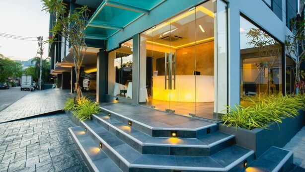 A modern building with a reception desk, glass doors, and a staircase leading to the entrance. - Garden View Apt- 1BR T1-103 (Chalong)