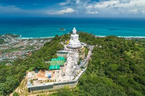 A large white pagoda surrounded by lush greenery and a coastal view. - Garden View Apt- 1BR T1-103 (Chalong)