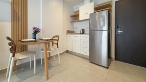 A modern kitchen with white cabinets, a stainless steel refrigerator, and a dining area with wooden chairs and a table. - Garden View Apt- 1BR T1-103 (Chalong)