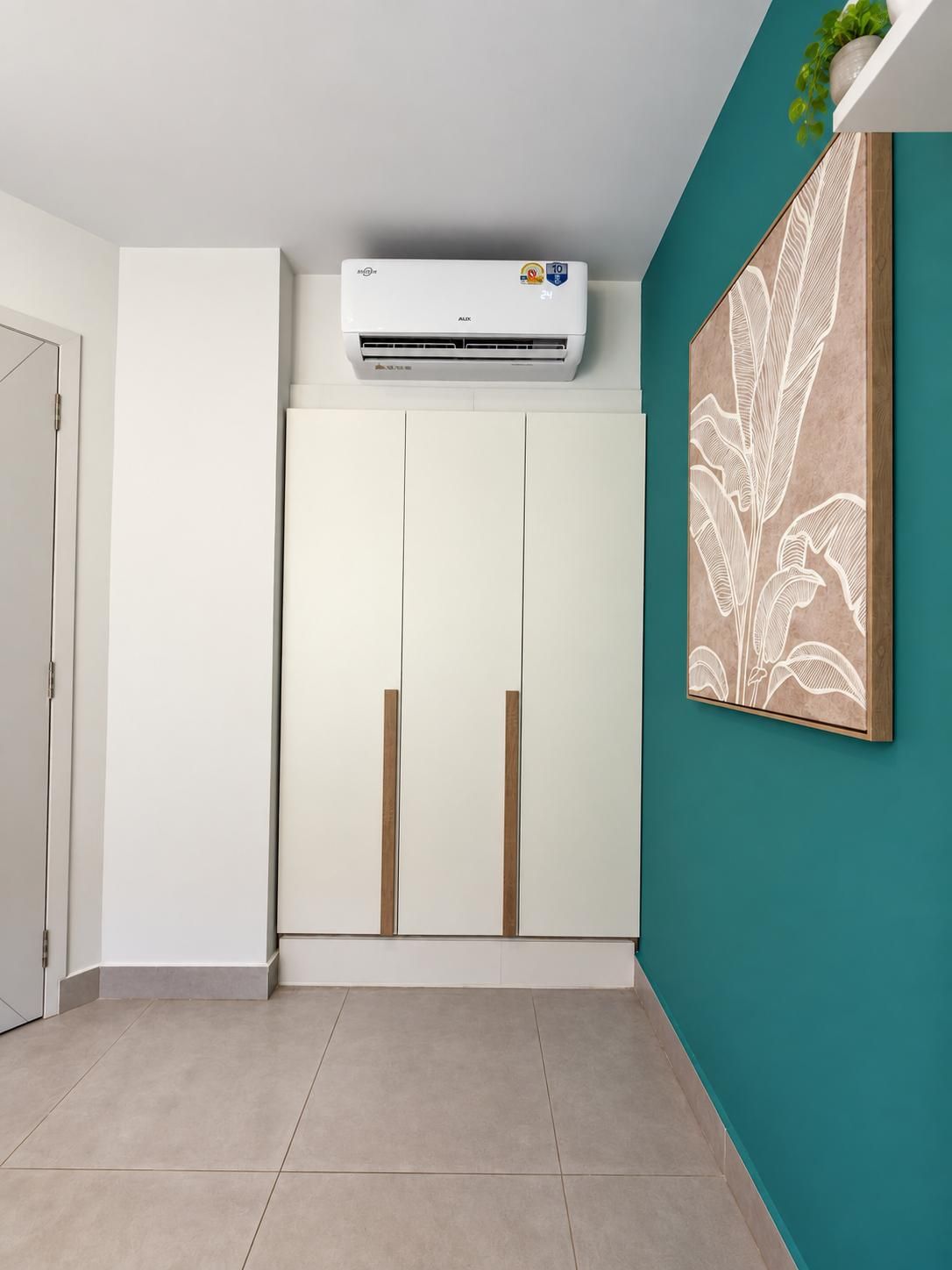 Ein Zimmer mit einem weißen Kleiderschrank, einer türkisblauen Akzentwand und einer weißen Klimaanlage.