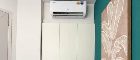 A room with a white wardrobe, a teal accent wall, and a white air conditioning unit.