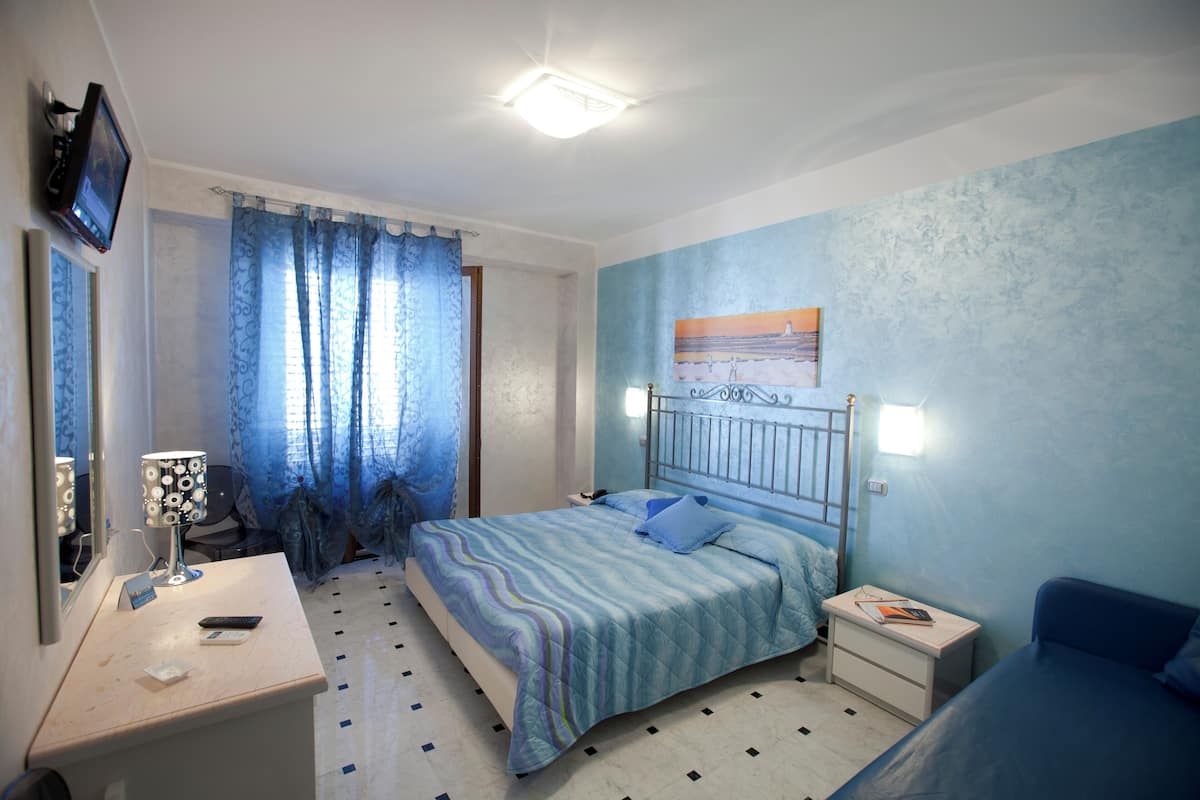 A bedroom with a bed, bedside tables, a desk, a chair, and a TV mounted on the wall.