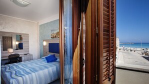 A bedroom with a bed, a desk, a chair, and a view of the beach. - Hotel Piccolo Mondo (San Vito Lo Capo)