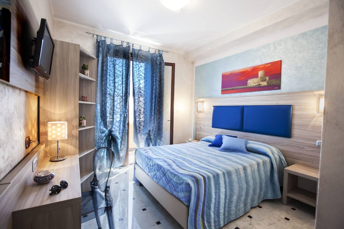 A modern bedroom with a large bed, a TV mounted on the wall, and a painting above the bed.