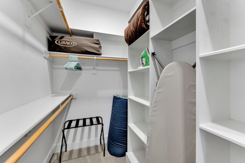 A narrow walk-in closet with shelves, a hanging bag, and a laundry basket.