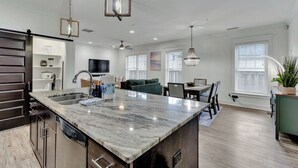 Una cocina moderna con una isla de mármol, electrodomésticos de acero inoxidable y un comedor con sofá verde y una araña.