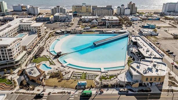 Vista aérea de un complejo turístico costero con una gran piscina, edificios frente a la playa y una vista despejada del océano.