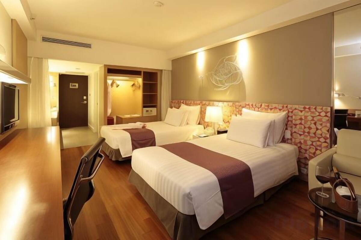 A hotel room with two beds, a desk, a chair, and a small table with a glass.