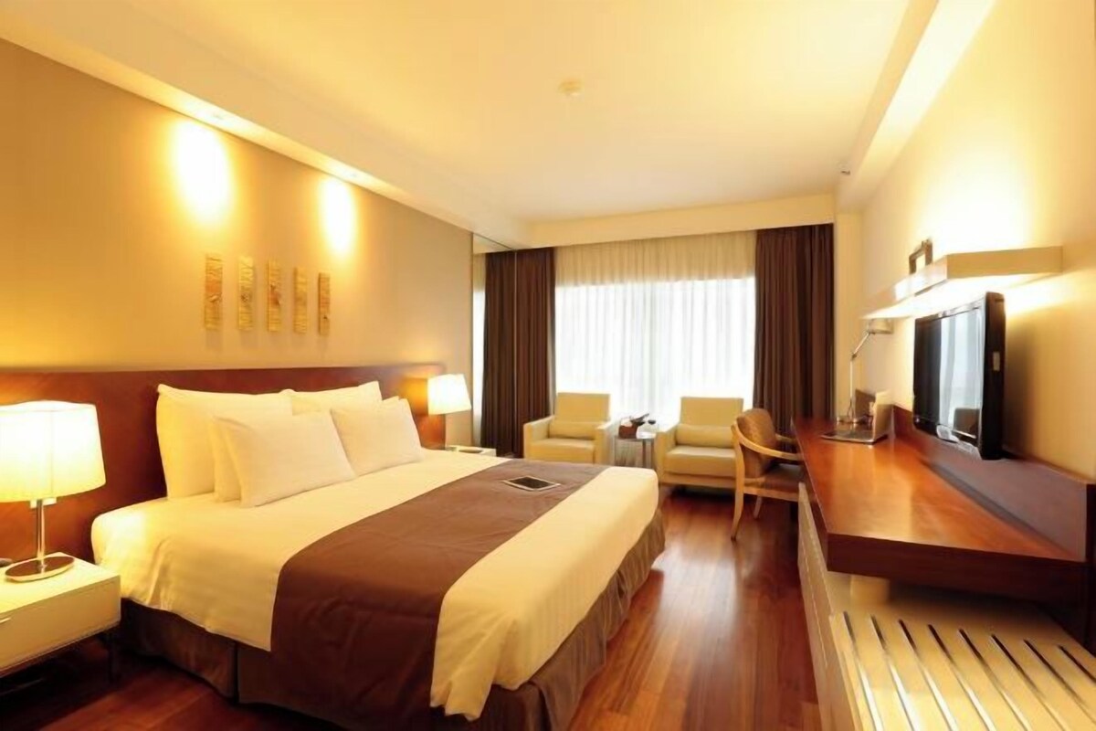 A hotel room with a large bed, a desk, a chair, a television, and a window with curtains.