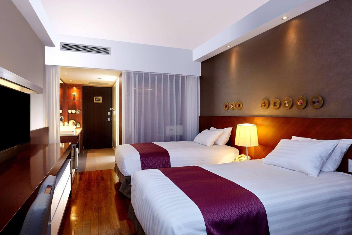 A hotel room with two beds, a TV, a desk, and a bathroom visible through a door.