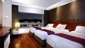 A hotel room with three beds, a desk, and a view of a cityscape at night. - Hotel Kukdo (Seoul)