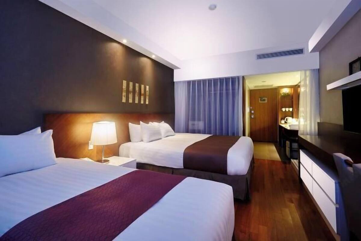 A hotel room with two beds, a desk, a chair, a TV, and a bathroom visible through a door.