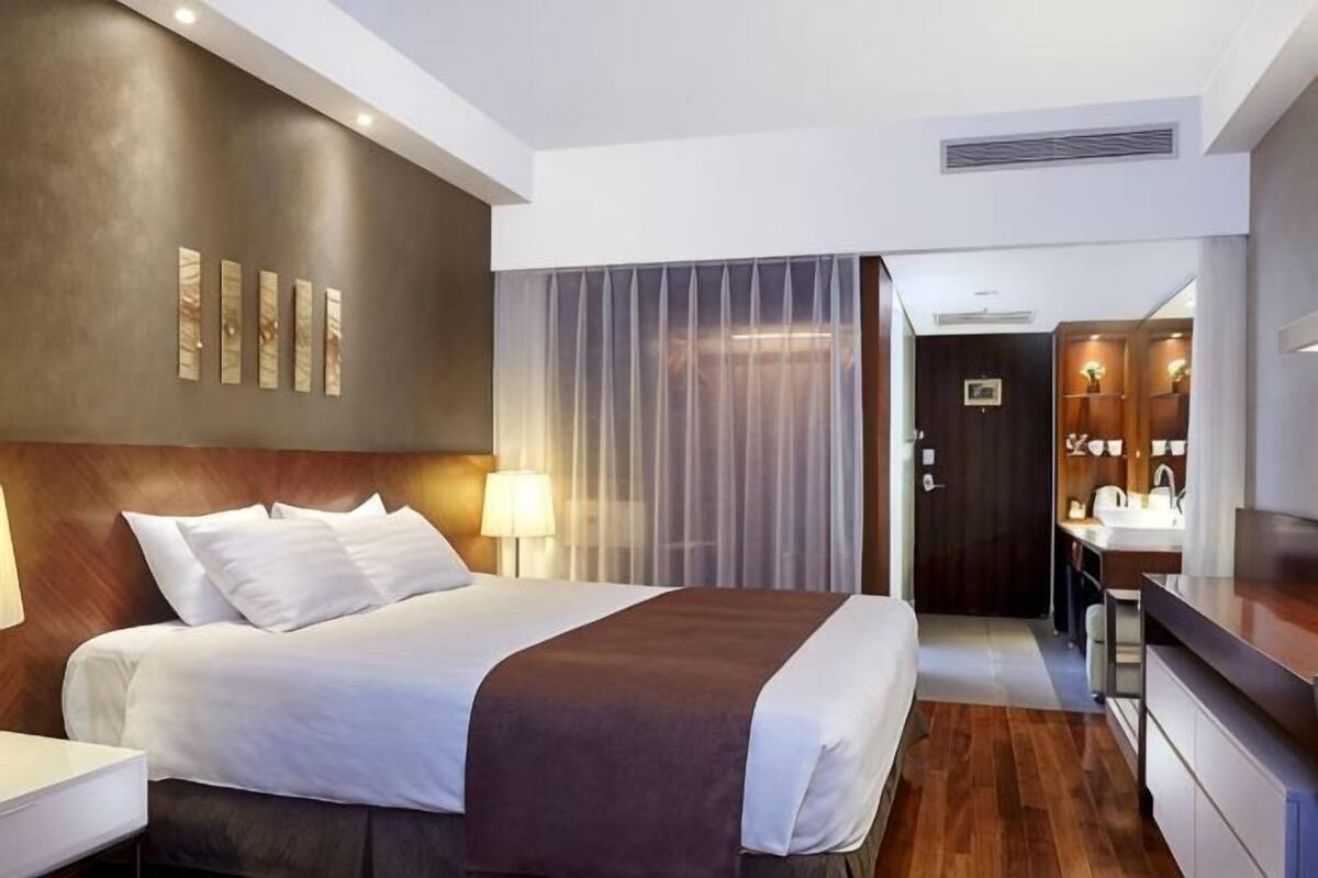 A hotel room with a bed, bedside table, lamp, and a view of the bathroom.