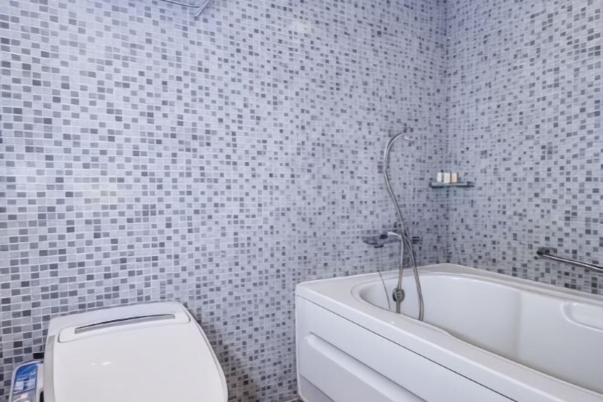 A bathroom with a tiled mosaic wall, a white bathtub, and a towel rack.