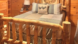 Un dormitorio de cabaña de madera con una cama, una mesita de noche, una lámpara y un ventilador de techo.