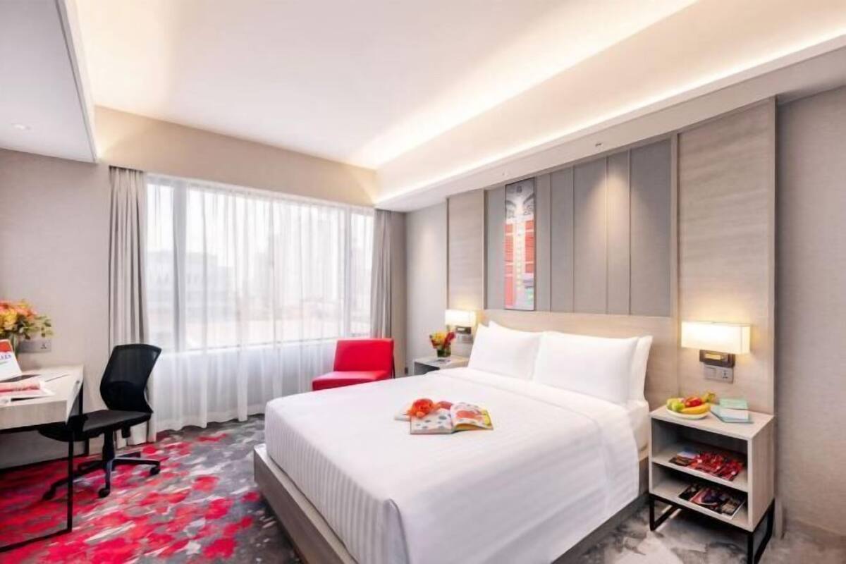 A hotel room with a bed, a desk, a chair, a nightstand, and a window with curtains.