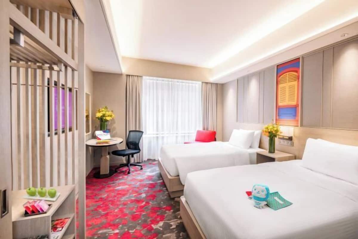 A hotel room with two beds, a desk with a chair, a small table with a vase of flowers, and a decorative wall piece.