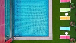 A swimming pool with a blue water feature, surrounded by a green lawn and colorful lounge chairs.