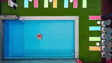 Una piscina con un objeto flotando, rodeada de un césped verde y una fila de toallas de colores.